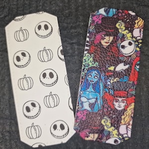 May include: Two fabric bookmarks featuring characters from the Nightmare Before Christmas. One bookmark has a white background with a repeating pattern of Jack Skellington's face and pumpkins. The other bookmark has a colorful background with characters from the movie, including Jack Skellington, Sally, and Oogie Boogie.