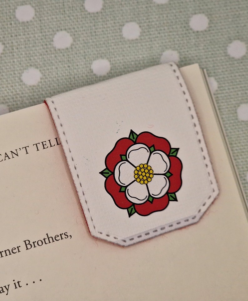 May include: White leather bookmark featuring a red and white rose design. The rose has a yellow centre and green leaves.