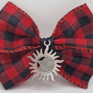 May include: A red and black plaid bow with a silver charm featuring a pentagram inside a sun.