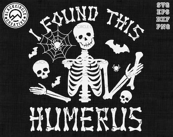 May include: A white graphic design on a black background featuring a skeleton holding a bone, surrounded by a spider web, spiders, bats, and two skulls. The text reads I FOUND THIS HUMERUS, with the letters styled to resemble individual bones.