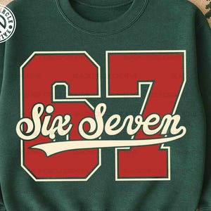 May include: A dark green sweatshirt featuring the number "67" in a bold red font with a white outline. The words "Six Seven" are written in a cursive font across the middle of the numbers. The sweatshirt has a crew neck.