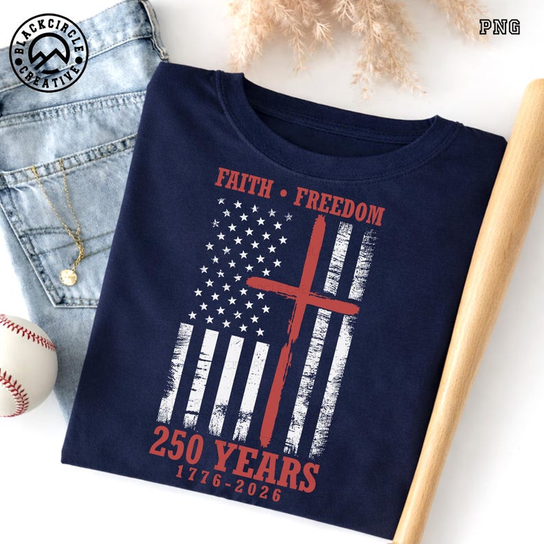 Puede incluir: Camiseta azul marino con un dise&ntilde;o desgastado de la bandera estadounidense y una cruz roja. Las palabras "Faith &bull; Freedom" est&aacute;n encima de la bandera, y "250 YEARS 1776-2026" debajo. La camiseta se muestra con una pelota de b&eacute;isbol, vaqueros y un bate.