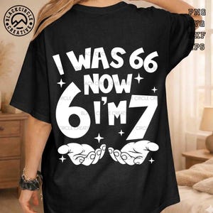 以下が含まれることがあります： 「I WAS 66 NOW I'M 7」の白い文字がプリントされた黒いTシャツ。白い星と手もデザインされています。カジュアルな普段着です。
