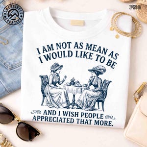 May include: A white t-shirt featuring a dark blue graphic of two people in Victorian-style clothing sitting at a table with tea. The text reads: I AM NOT AS MEAN AS I WOULD LIKE TO BE AND I WISH PEOPLE APPRECIATED THAT MORE. The design is centered.