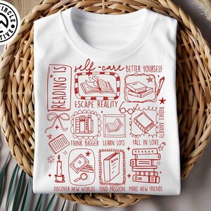 May include: White t-shirt with a red graphic design featuring book-related illustrations and text. The design includes phrases like "Reading is," "Self-care," and "Escape Reality." The shirt is displayed on a woven basket.