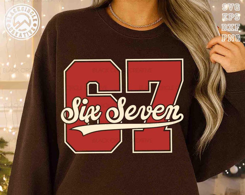 May include: A brown sweatshirt featuring the number "67" in a bold, red, collegiate-style font with a white outline. Below the number, the words "Six Seven" are written in a cursive font with a white banner. The design is centered on the chest.