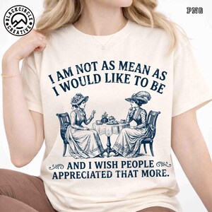 May include: A cream-colored t-shirt featuring a dark blue vintage-style illustration of two people in Victorian-era clothing sitting at a table with tea. The text reads: I AM NOT AS MEAN AS I WOULD LIKE TO BE AND I WISH PEOPLE APPRECIATED THAT MORE.