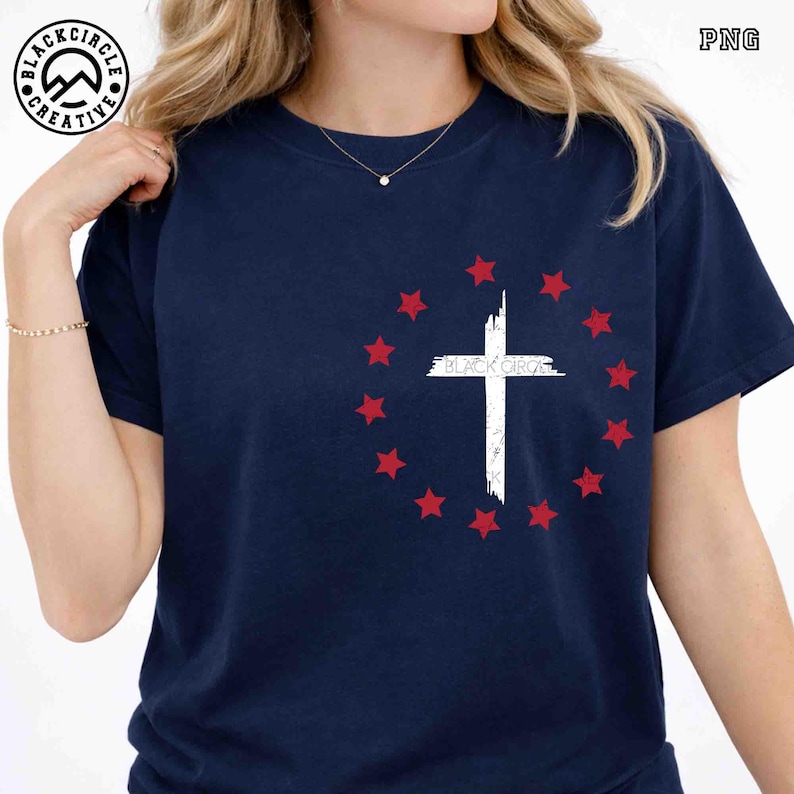 May include: Navy blue t-shirt featuring a white cross design encircled by red stars. The text "BLACK CIRCLE" is printed on the cross. The shirt is a casual wear item.
