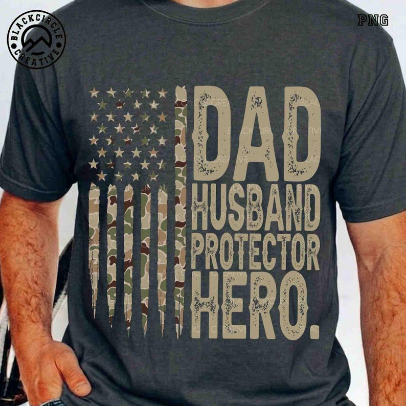 Puede incluir: Camiseta gris oscuro con un dise&ntilde;o de bandera americana desgastada, con rayas y estrellas de camuflaje. La camiseta muestra las palabras "DAD, HUSBAND, PROTECTOR, HERO" en una fuente beige texturizada. Una idea de regalo patri&oacute;tico.