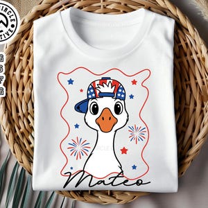 May include: White t-shirt with a red, white, and blue cartoon goose wearing a red, white, and blue baseball cap. The goose is wearing a red, white, and blue baseball cap with stars. The text "Mateo" is printed below the goose.
