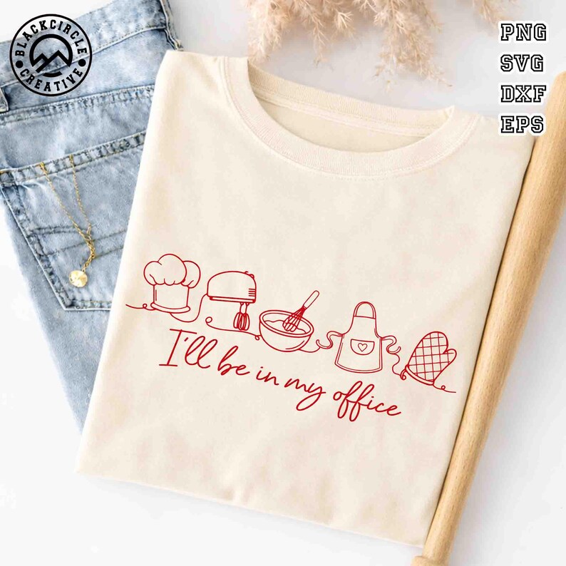 Puede incluir: Camiseta color crema con un dibujo lineal rojo de utensilios de reposter&iacute;a y el texto "I'll be in my office". El dise&ntilde;o incluye un gorro de chef, batidora, cuenco con batidor, delantal y manopla. La camiseta est&aacute; doblada junto a unos vaqueros.