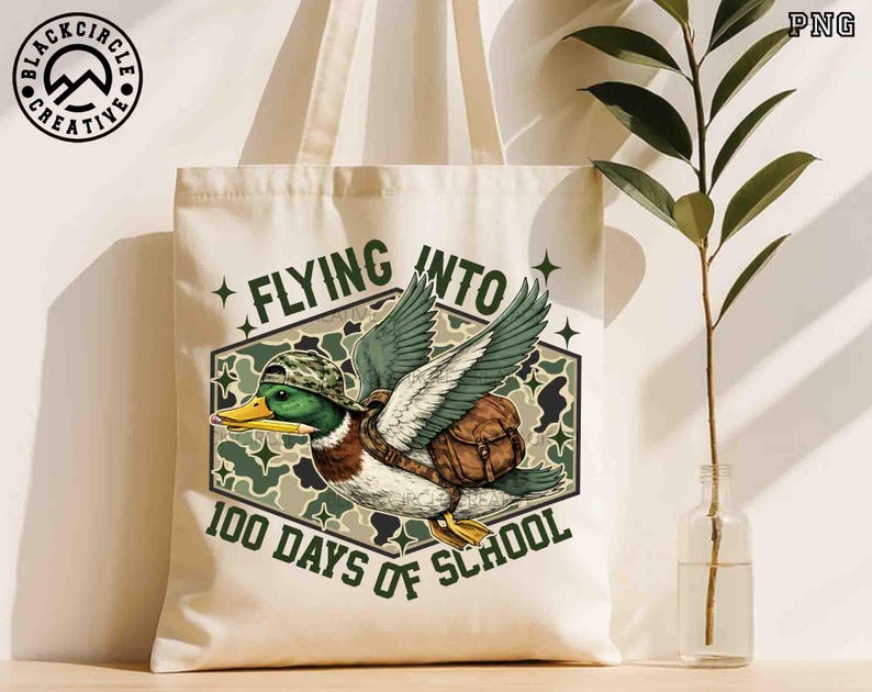 Pu&ograve; includere: Borsa tote color crema con un'anatra dei cartoni animati con cappello e zaino mimetico, con una matita nel becco. Il testo recita "Flying Into 100 Days of School". La borsa ha un logo Black Circle Creative.