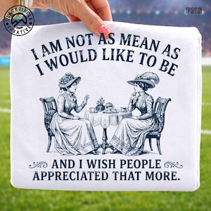 May include: A white t-shirt featuring a dark blue graphic of two people in Victorian-style clothing sitting at a table with tea, with the text: I AM NOT AS MEAN AS I WOULD LIKE TO BE AND I WISH PEOPLE APPRECIATED THAT MORE.