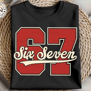 May include: Black t-shirt featuring a red and white graphic of the number "67" with the words "Six Seven" in a vintage font. The design has a retro, collegiate style. The shirt is displayed on a woven surface.