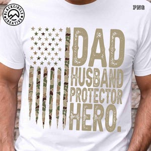 Puede incluir: Camiseta blanca con un dise&ntilde;o de bandera americana de camuflaje. La camiseta tiene las palabras "DAD, HUSBAND, PROTECTOR, HERO" en una fuente desgastada. Ideal para el D&iacute;a del Padre o para celebrar a un padre.