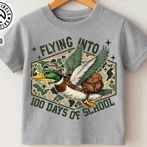 Pu&ograve; includere: T-shirt grigia con un'anatra dei cartoni animati con cappello e zaino mimetico, che vola con le ali spiegate. Il testo "FLYING INTO 100 DAYS OF SCHOOL" &egrave; visualizzato in un esagono con sfondo mimetico. La maglietta ha girocollo e maniche corte.