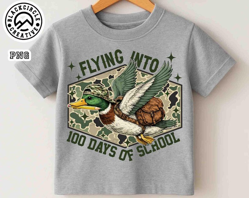 Pu&ograve; includere: T-shirt grigia con un'anatra dei cartoni animati con cappello e zaino mimetico, che vola con le ali spiegate. Il testo "FLYING INTO 100 DAYS OF SCHOOL" &egrave; visualizzato in un esagono con sfondo mimetico. La maglietta ha girocollo e maniche corte.