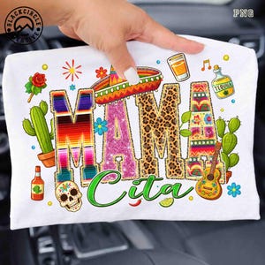 Op de afbeelding: Wit T-shirt met de woorden "MAMA Cita" in kleurrijke, decoratieve letters. Het ontwerp bevat een sombrero, een tequila fles, een gitaar, een cactus en een schedel, allemaal in een feestelijke, Mexicaans geïnspireerde stijl.