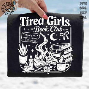 Può includere: T-shirt nera con un design grafico bianco. Il design presenta il testo "Tired Girls Book Club" insieme a libri, candele, una tazza di caffè e una fiamma, con la frase "Running on coffee, chaos, and chapters."