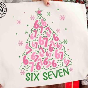 May include: A white tote bag featuring a Christmas tree design made of the numbers 6 and 7 in pink. The tree is outlined in green with green snowflakes and stars. The words "SIX SEVEN" are printed in green at the bottom.
