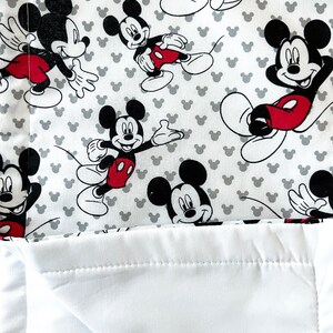 May include: White and gray fabric with a repeating pattern of Mickey Mouse. The fabric has a white backing.