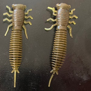 May include: Two brown and green segmented fishing lures with multiple legs. The lures are made of soft plastic and have a segmented body.