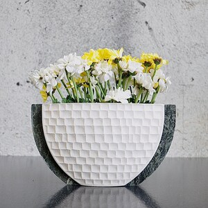 Op de afbeelding: Een witte keramische kom met een groene marmeren rand, gevuld met witte en gele madeliefjes. De kom heeft een getextureerd, geruit patroon.