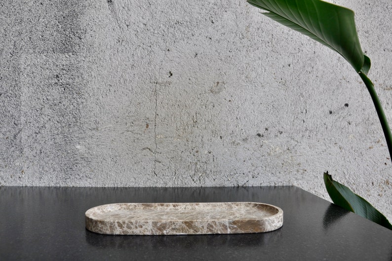 May include: A light brown oval marble tray with a textured surface. The tray is sitting on a black surface.