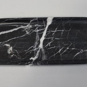 May include: A black marble oval tray with white veining. The tray is smooth and polished.