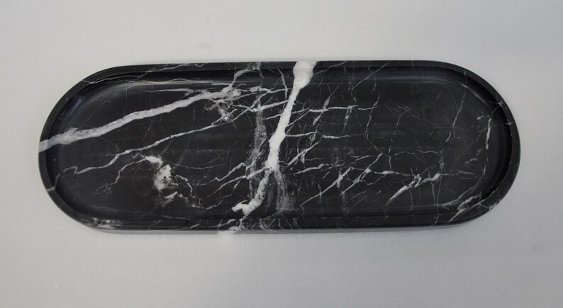 May include: A black marble oval tray with white veining. The tray is smooth and polished.