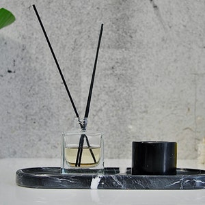 May include: A black marble tray with a clear glass bottle of diffuser sticks and a black candle. The tray is on a white surface.