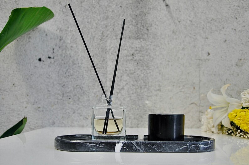 May include: A black marble tray with a clear glass bottle of diffuser sticks and a black candle. The tray is on a white surface.