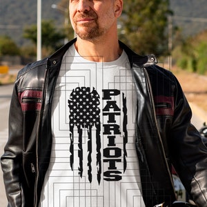May include: A white t-shirt with a black and white distressed American flag design and the word "PATRIOTS" printed vertically on the right side of the flag.