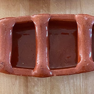 May include: A terracotta serving dish with three divided sections. The dish is oval shaped and has a rustic, handmade appearance.