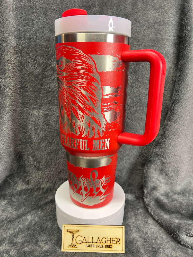 May include: Red stainless steel travel mug with a red lid and handle. The mug features a silver eagle design with the words "The Few, The Proud, The Fearful Men" engraved on it.