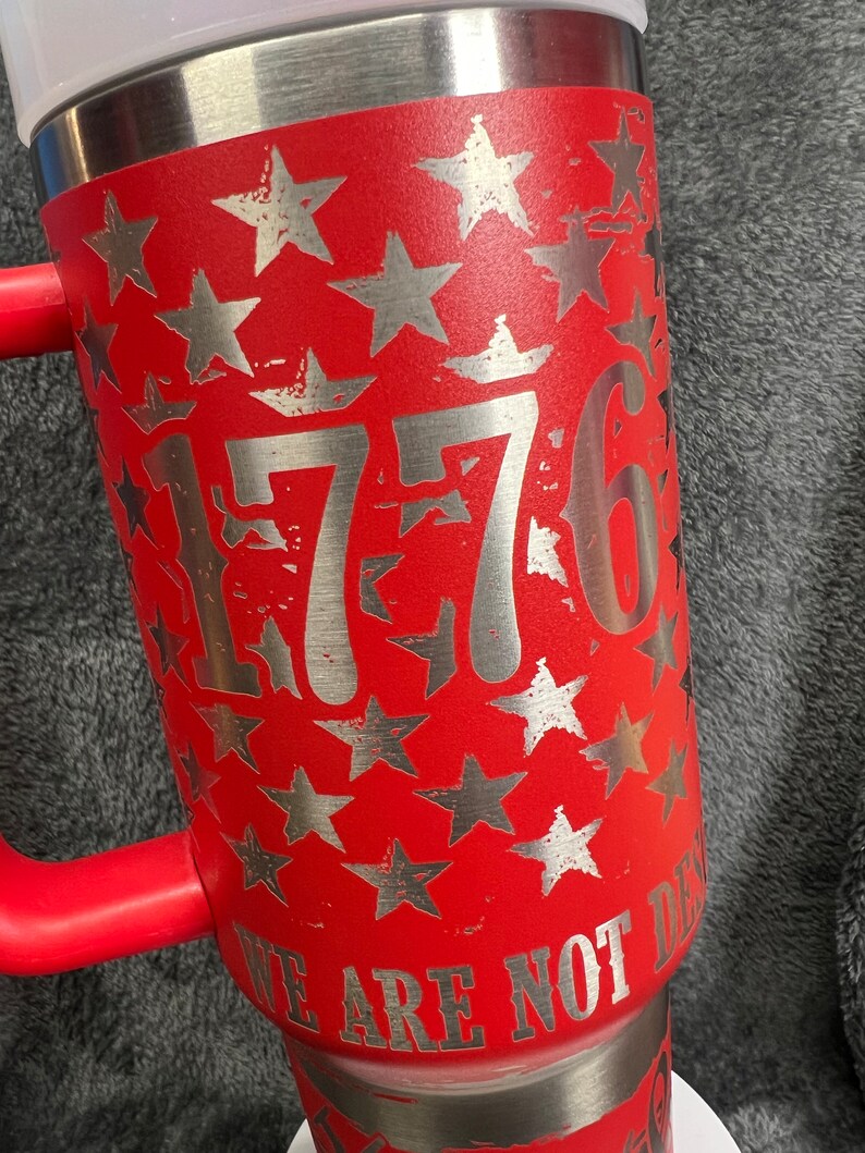 May include: Red stainless steel tumbler with a silver design of stars and the number 1776. The text "We Are Not Done" is printed on the bottom of the tumbler.