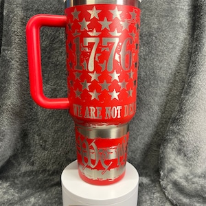 May include: Red stainless steel travel mug with a red handle and a white lid. The mug features a silver design of stars and the number 1776. The text "We are not done yet" is also on the mug.