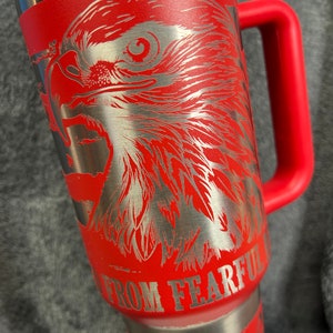 May include: Red stainless steel travel mug with a silver eagle design and the text "Do Not Go Gentle Into That Good Night" and "From Fearful" on the side.