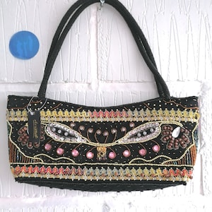 May include: Black beaded handbag with a decorative design. The bag has a beaded handle and is decorated with sequins, pink gems, and gold and brown beads. A tag is attached to the handle.