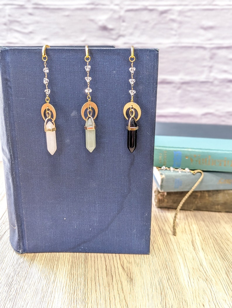 May include: Three gold crystal bookmarks with a crescent moon charm and a crystal point. The crystals are clear, green, and black.