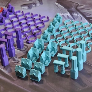 May include: An assortment of colorful game pieces, including miniature houses, arches, and cylindrical structures. The pieces are in shades of red, purple, and teal, arranged on a patterned surface, likely for a board game.