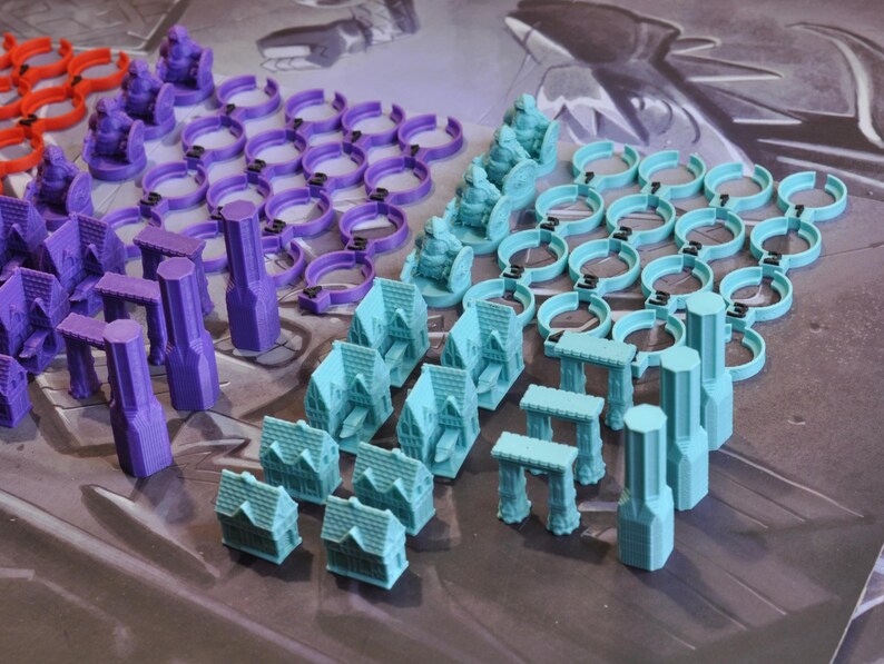 May include: An assortment of colorful game pieces, including miniature houses, arches, and cylindrical structures. The pieces are in shades of red, purple, and teal, arranged on a patterned surface, likely for a board game.