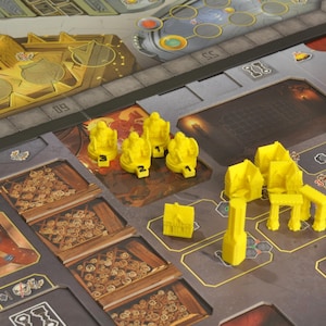 May include: A board game with a detailed game board featuring various sections and yellow game pieces. The board has a metallic look with brown and gray tones. Yellow game pieces include figures, chairs, and other structures. The game appears to be a strategy or resource management game.