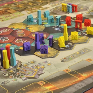 May include: A board game with a detailed game board featuring hexagonal tiles and various colorful game pieces. The pieces include miniature buildings and abstract shapes in shades of blue, red, yellow, and purple. The game board has a detailed design with various symbols and markings.