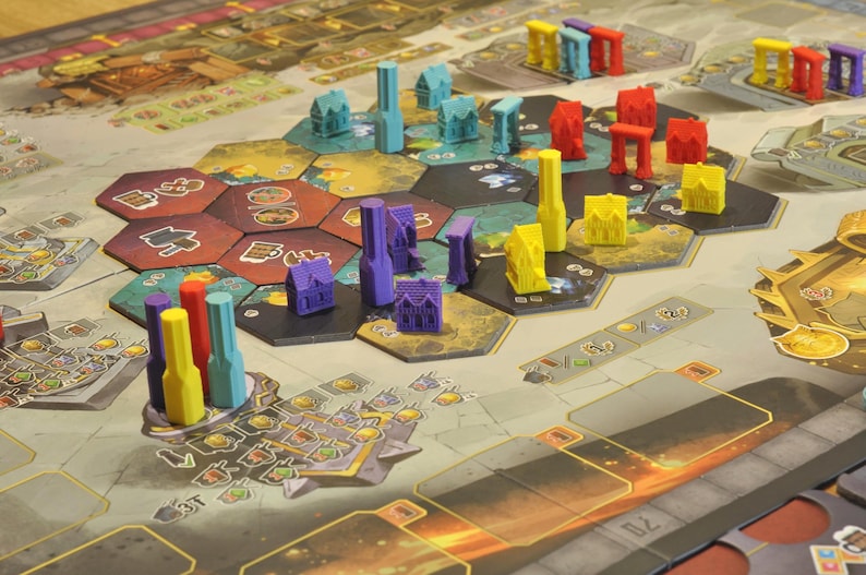 May include: A board game with a detailed game board featuring hexagonal tiles and various colorful game pieces. The pieces include miniature buildings and abstract shapes in shades of blue, red, yellow, and purple. The game board has a detailed design with various symbols and markings.