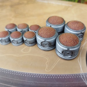 Puede incluir: Un conjunto de nueve dados de juego plateados y marrones con una superficie texturizada y un símbolo de infinito en cada dado.