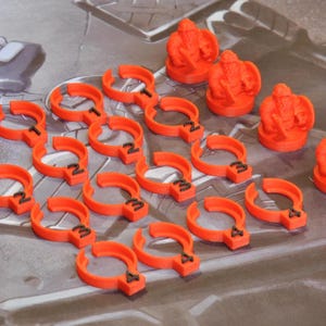 May include: Orange game pieces, including crown-shaped figures and curved pieces with numbers, are arranged on a game board. The pieces are bright orange and appear to be made of plastic. The game board has a gray and brown color scheme.