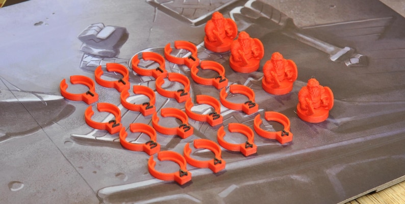 May include: Orange game pieces, including crown-shaped figures and curved pieces with numbers, are arranged on a game board. The pieces are bright orange and appear to be made of plastic. The game board has a gray and brown color scheme.