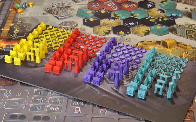 May include: A board game setup with various colorful game pieces. Yellow, red, purple, and teal pieces are arranged in rows. The game board features hexagonal tiles and detailed artwork, suggesting a strategy or resource management theme.