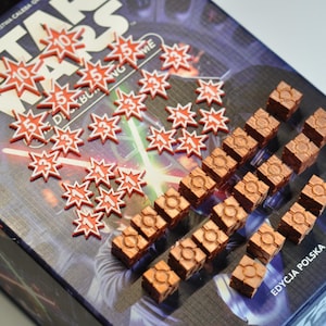 Puede incluir: Primer plano de una caja de juego de Star Wars con dados rojos y blancos y cubos de color cobre. La caja tiene las palabras "Star Wars" impresas en ella en letras blancas.